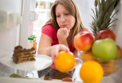 woman standing in front of fridge choosing between fruit and cake