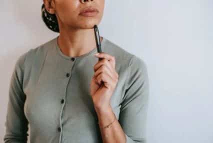 woman holding a pen to her chin with a ponderous look on her face