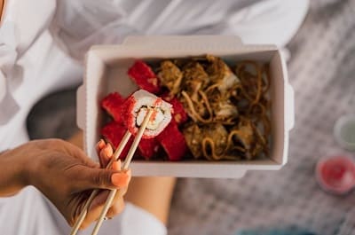 woman holding a piece of sushi with chopsticks above a beautiful plate of Asian food to symbolize eating to both fullness and satisfaction
