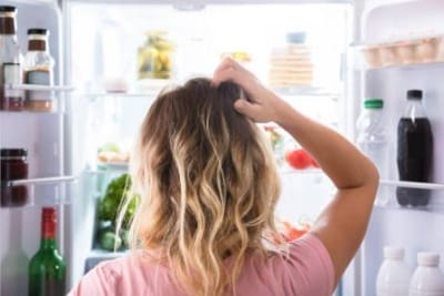 woman standing in front of refrigerator to symbolize the reason why I feel full but not satisfied after eating